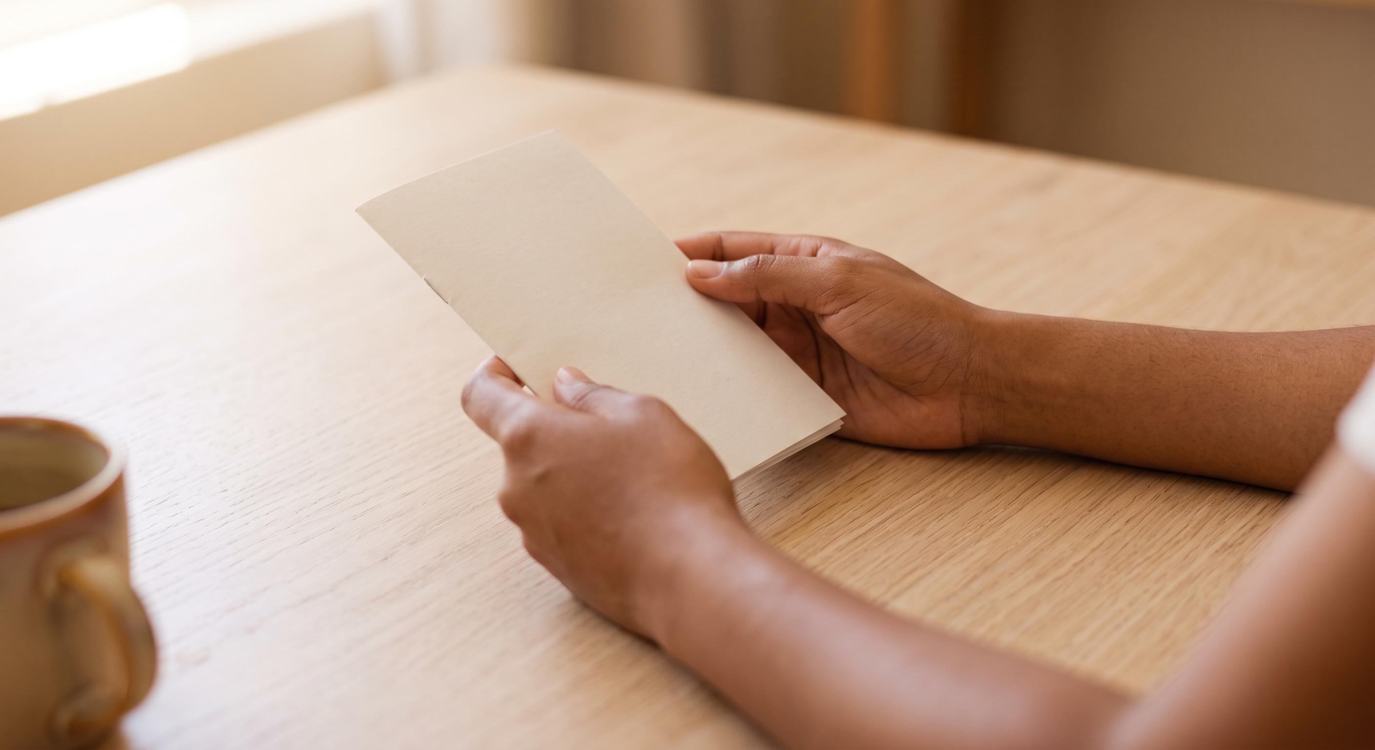 Hands holding a plain booklet at a kitchen table